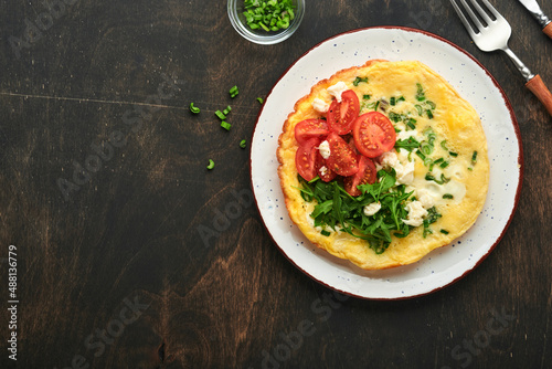 Rustic omelette or frittatas with green onions, cheese mozzarella, green arugula and tomatoes on old wooden dark background. Healthy food concept. Breakfast. Copy space. Top view. Mock up.