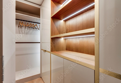 Fashionable wooden dressing room with luminous lamps and parquet on the floor, lockers, shelves and hangers.
