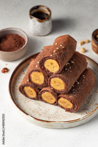 Rolled vegan chocolate crepes with banana and nuts on ceramic plate. Vegan, plant based food. vertical image