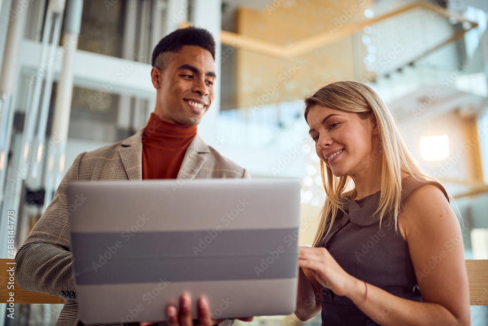 Close-up of two young colleagues who are watching a laptop content while standing in the hallway. Business, people, company