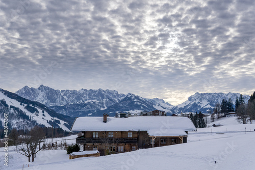 wooden house, cabin in the snow with mountains and nice cloudy sky during sunset