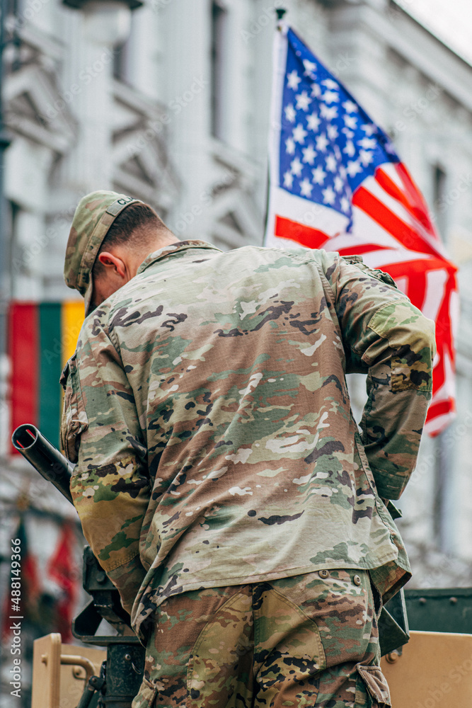 Fototapeta premium United States Marine Corps soldier on the top of a military vehicle mounting a machine gun with American and Lithuanian flag, USA or US army, NATO response force, vertical