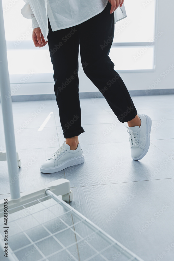 Women's legs in black trousers and white leather sneakers. Modern casual style. New shoe collection Women's legs in black trousers and white leather sneakers. Modern casual style. New shoe collection