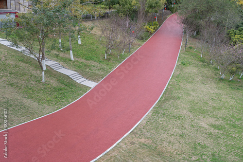 The red asphalt runway in the modern city park is surrounded by green plants on both sides