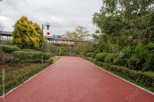 The red asphalt runway in the modern city park is surrounded by green plants on both sides