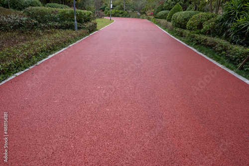 The red asphalt runway in the modern city park is surrounded by green plants on both sides