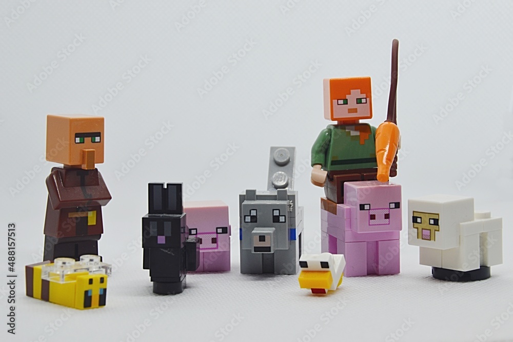 LEGO Minecraft Alex riding on pig mob with carrot on fishing rod, villager  on the left with rabbbit, bee, wolf, rabbit, chicken and sheep also  present. Stock Photo