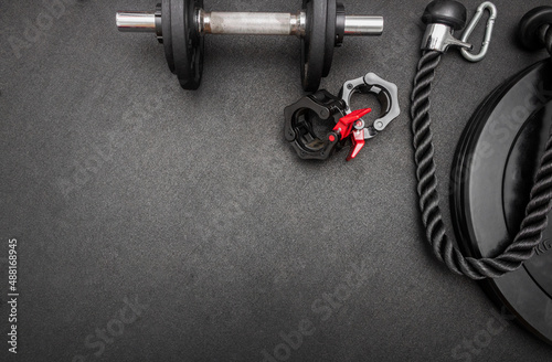Barbell, dumbbells, triceps rope and clamps on the floor at the gym. Top down view flat lay with bodybuilding equipment on a black background and empty space for text. Fitness, weight training concept