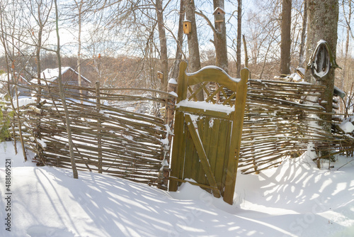 Wooden fence made of sticks with a wooden door in the yard in winter