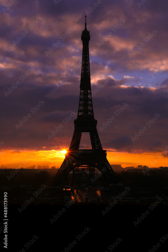 Silhouette of the Eiffel tower with dramatic sky in the background. Orange clouds at sunset or sunrise. Vertical plan.