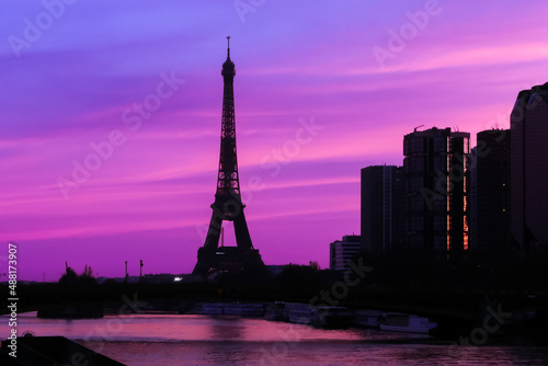 View on the Eiffel tower with group of modern buildings in front of the water of Seine river. Dramatic sky with colorful clouds. Silhouette of a cityscape at sunrise. © Bruno