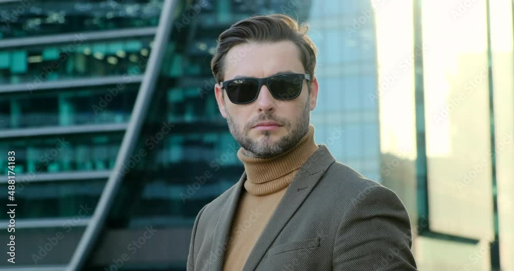 a successful businessman in a brown suit and a turtleneck against the backdrop of a business center of skyscrapers turns his head to the camera and looks confidently in sunglasses. New York, USA