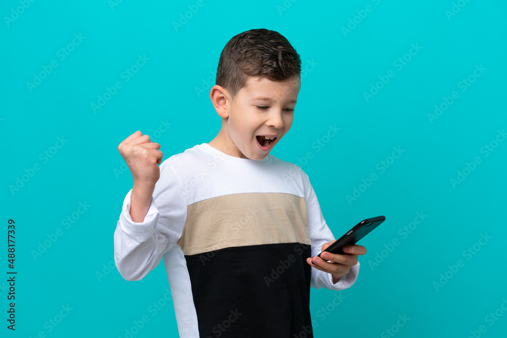 Little kid boy isolated on blue background with phone in victory position Little kid boy isolated on blue background with phone in victory position