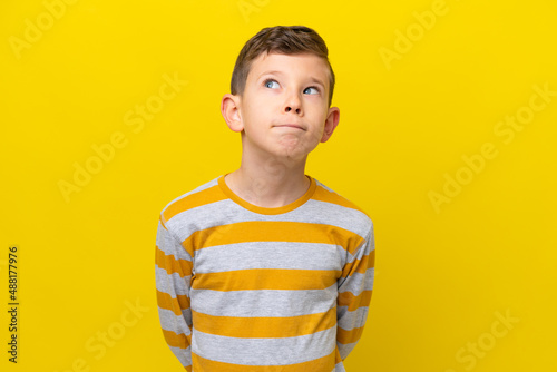 Little caucasian boy isolated on yellow background and looking up