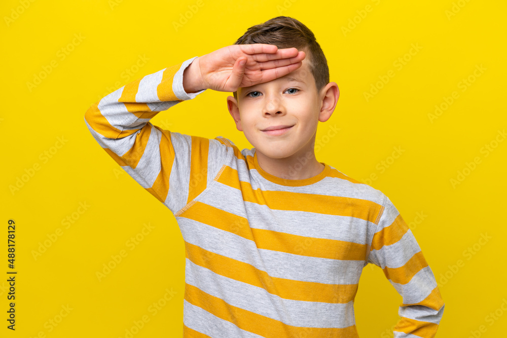 Little caucasian boy isolated on yellow background saluting with hand with happy expression Little caucasian boy isolated on yellow background saluting with hand with happy expression