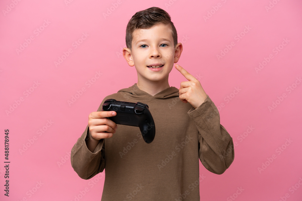 Little caucasian boy playing with a video game controller isolated on pink background giving a thumbs up gesture Little caucasian boy playing with a video game controller isolated on pink background giving a thumbs up gesture