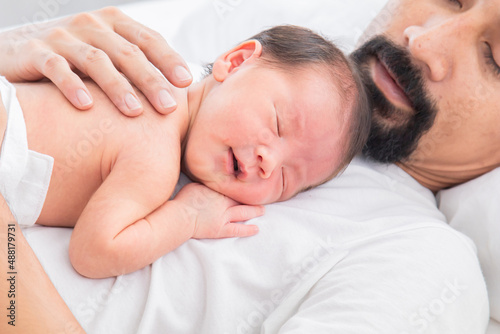 Close up of Asian newborn baby sleeping on his father's chest. Dad and son spend time together at home, young dad with cute little infant in his arms. Father and toddler in bed in the morning