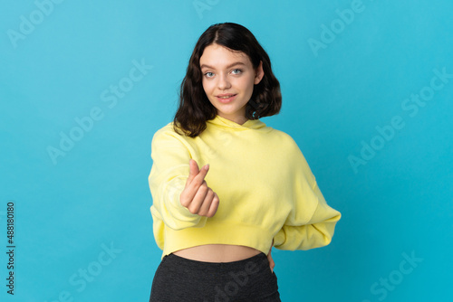 Teenager Ukrainian girl isolated on blue background making money gesture