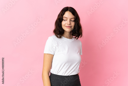 Teenager Ukrainian girl isolated on pink background having doubts while looking side