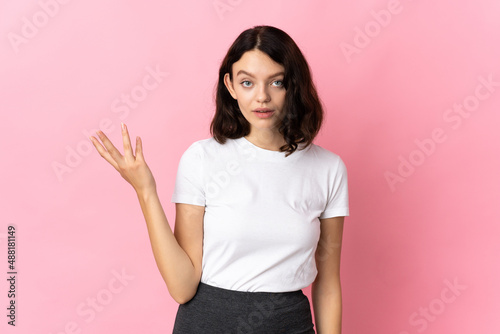 Teenager Ukrainian girl isolated on pink background making doubts gesture