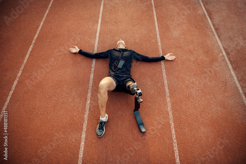 Top view of a fit handicapped sportsman lying down on the running track and relaxing with music. © dusanpetkovic1