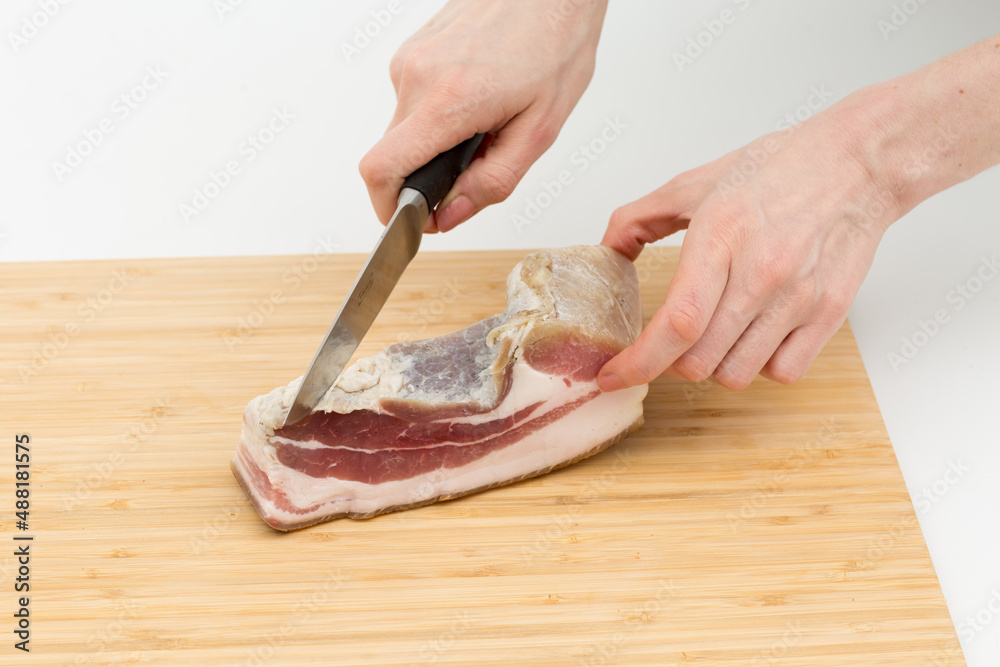 two hands cut the bacon on the board