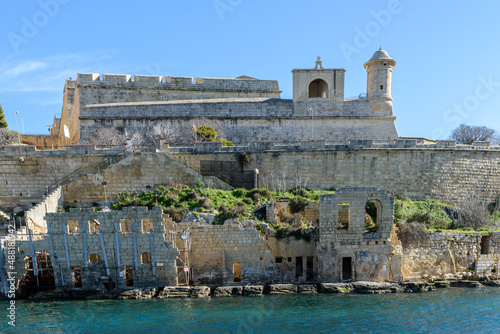 Derelict buildings on the shore of Marsamxett Harbour, Valletta, Malta. In the background is Saint Michael's Counterguard, with its small chapel dedicated to St. Roche. photo