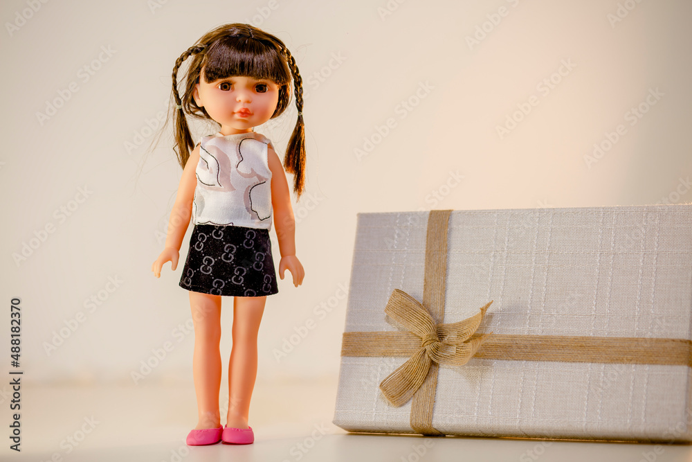 Creative and fashionable photoshoot of adorable doll standing next to the gift