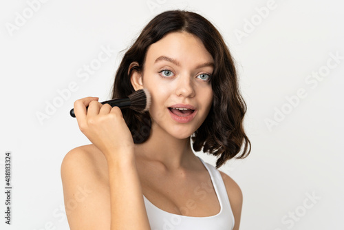Teenager Ukrainian girl isolated on white background holding makeup brush and surprised