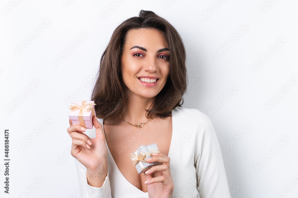 Young woman in a cocktail dress, gold chain, bright spring pink makeup on a white background. Holds a gift box for March 8 and smiles cheerfully. Young woman in a cocktail dress, gold chain, bright spring pink makeup on a white background. Holds a gift box for March 8 and smiles cheerfully.