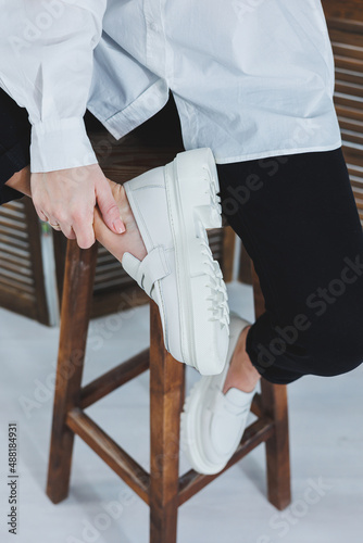 Legs of a young beautiful woman in black trousers and modern stylish white leather loafers. New collection of women's shoes spring-summer 2022