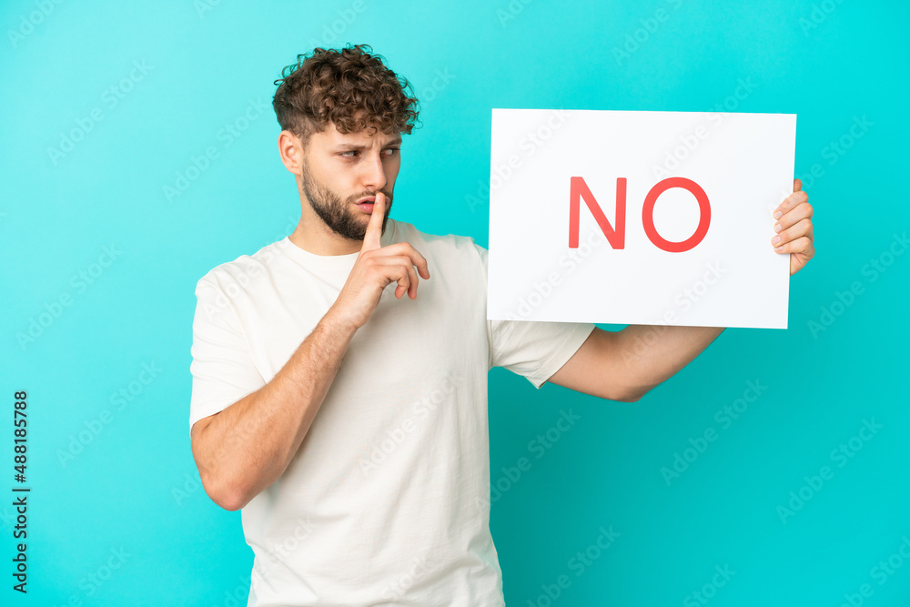 Young handsome caucasian man isolated on blue background holding a placard with text NO doing silence gesture Young handsome caucasian man isolated on blue background holding a placard with text NO doing silence gesture