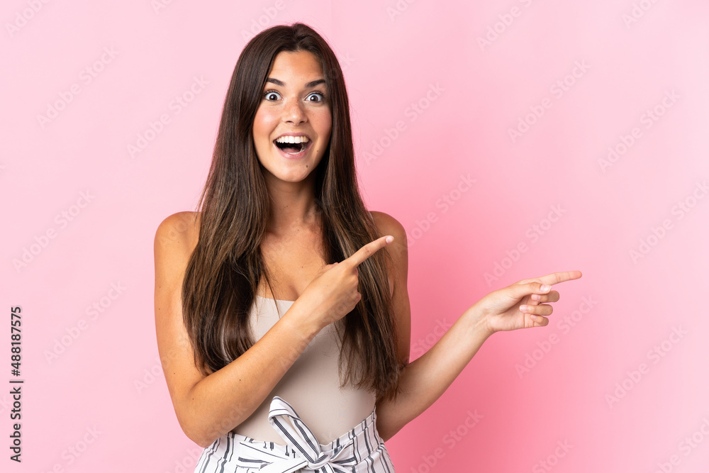 Young brazilian woman isolated on pink background surprised and pointing side Young brazilian woman isolated on pink background surprised and pointing side