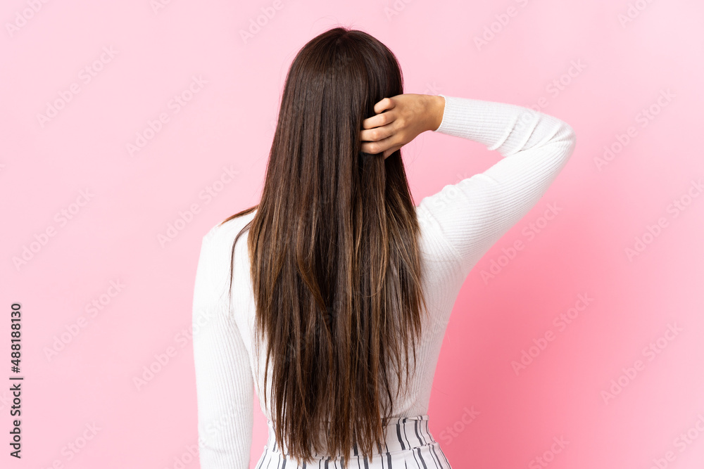 Young brazilian woman isolated on pink background in back position and thinking Young brazilian woman isolated on pink background in back position and thinking