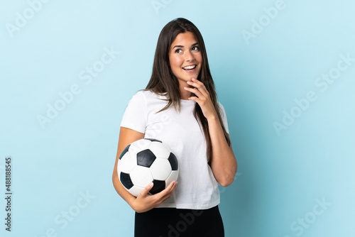 Young football player brazilian girl isolated on blue background looking up while smiling © luismolinero