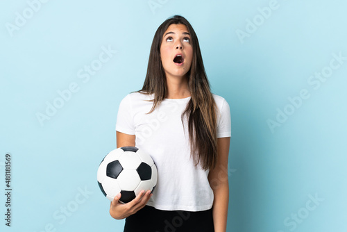 Young football player brazilian girl isolated on blue background looking up and with surprised expression © luismolinero