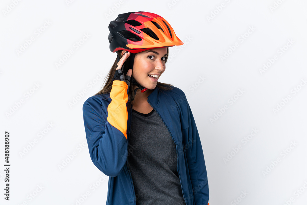 Fototapeta premium Young cyclist brazilian girl isolated on white background listening to something by putting hand on the ear