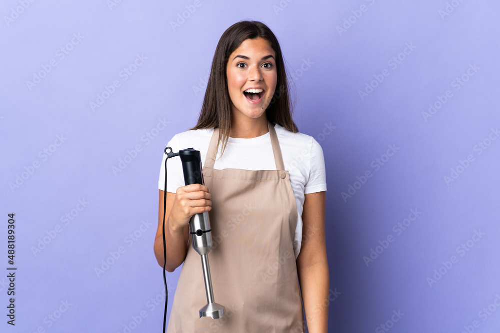 Brazilian woman using hand blender isolated on purple background with surprise facial expression