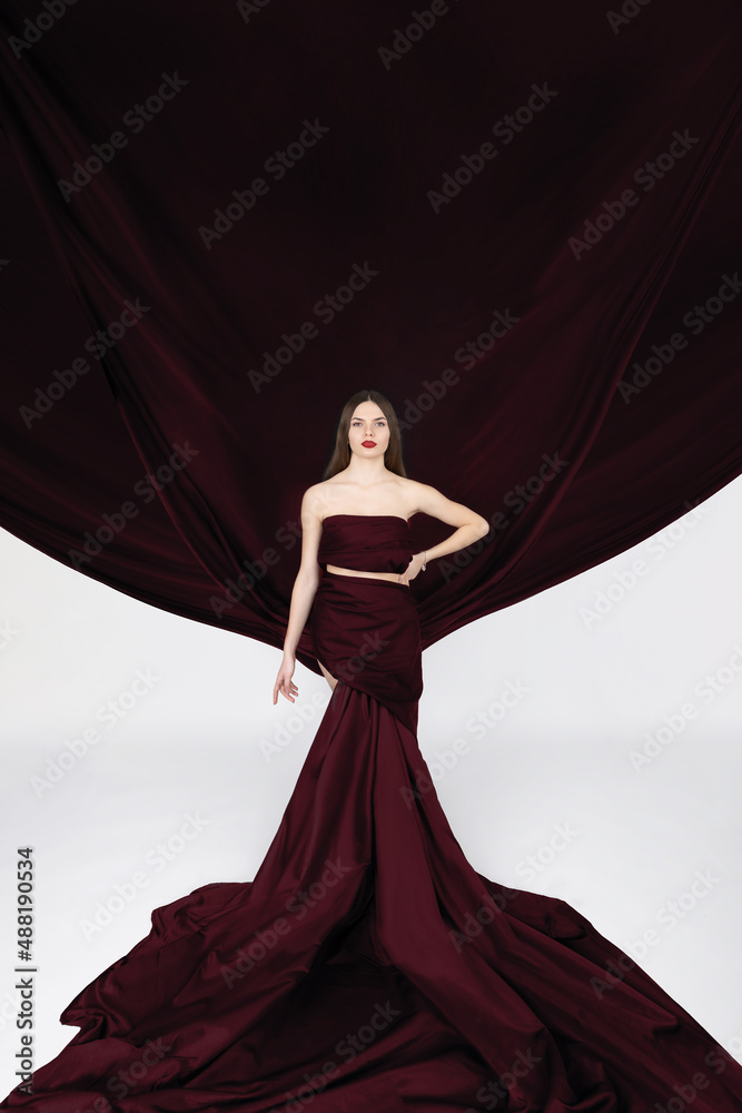Fashion, fine art, fantasy concept. Beautiful long brown hair woman with red lips wearing huge red dress with flying trails like wings in white background with copy space. Image with motion blur Fashion, fine art, fantasy concept. Beautiful long brown hair woman with red lips wearing huge red dress with flying trails like wings in white background with copy space. Image with motion blur