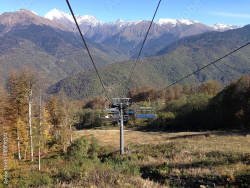 Ski lift chairs in front of the beautiful autumn trees and high mountains. Transit. Transportation. Autumn. Fall