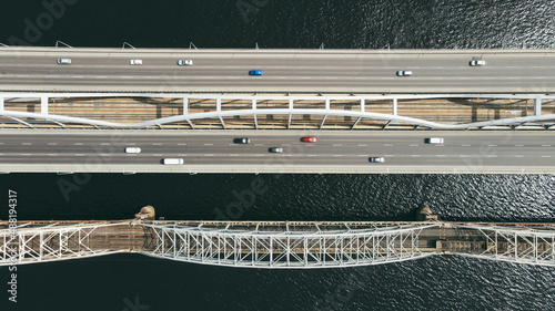 Aerial top view of cars and train passing the bridge over the river in the city