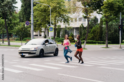 Friends in sportswear running in the city dicussing on pedestrian street. Multiethnic women having a fitness workout. © arthurhidden