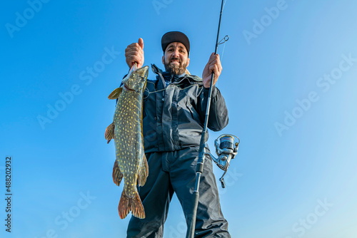 Success pike fishing. Happy fisherman with big fish trophy and spinning rod tackle photo