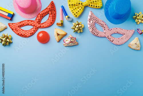 Purim holiday concept with carnival mask, noisemaker, hamantaschen cookies and party supplies on blue background. Top view, flat lay composition