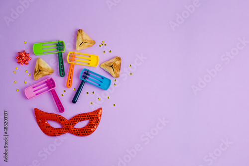 Purim holiday background with carnival mask, noisemaker and hamantaschen cookies. Top view with copy space photo
