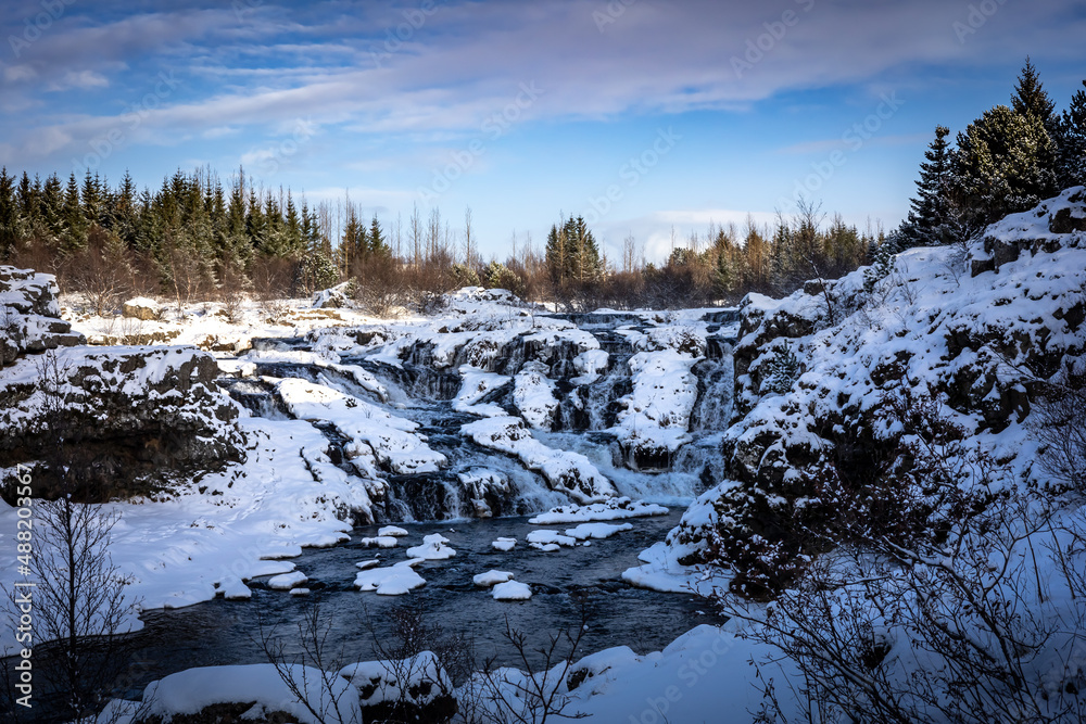 Kermoafoss waterfall in winter, surrounded by the forest in Reykjavik, Iceland. 