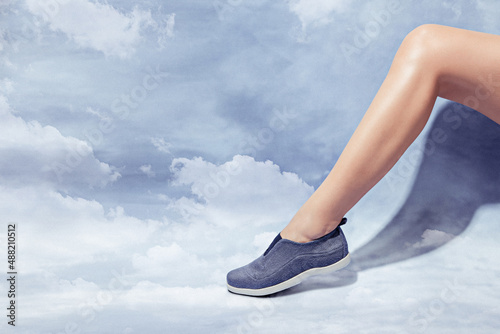 Woman leg in stylish blue sneaker isolated on cloud sky background, space for text