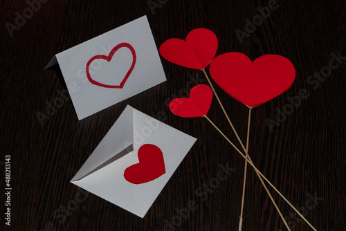 Three cardboard hearts on the rays of sticks intersect at one point. A love letter with a red heart and an envelope with a heart seal, surrounded by hearts, for Valentine's Day.