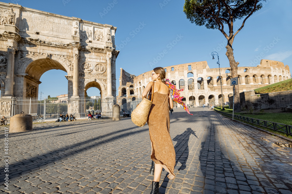 Woman walks near Coliseum and Constantine Arch in Rome. Caucasian woman wearing summer dress and colorful shawl in hair. Concept of italian style and travel