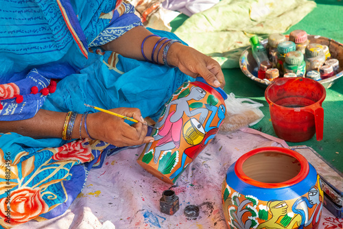 Rural Indian woman in traditional costume painting a clay vase for sale at handicraft fair at Kolkata, India